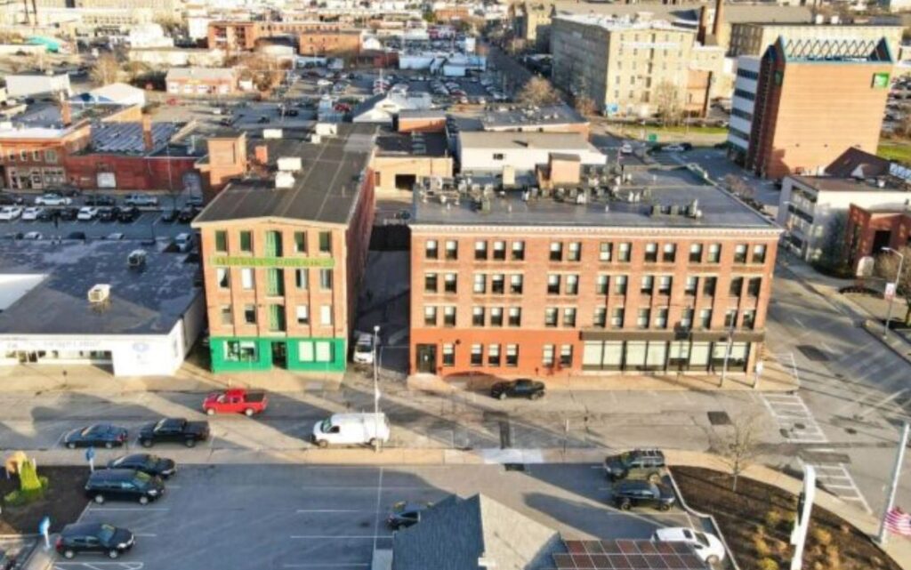 Aerial view of urban buildings, parking lots, and streets in a city setting.