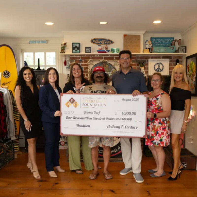 Group of six people holding a large donation check for $4,900 in a colorful store setting.