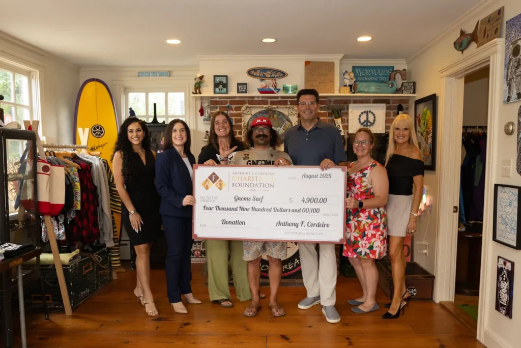 Group of six people holding a large donation check for $4,900 in a colorful store setting.