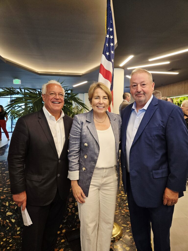 Three people pose together in a modern setting, with an American flag in the background.