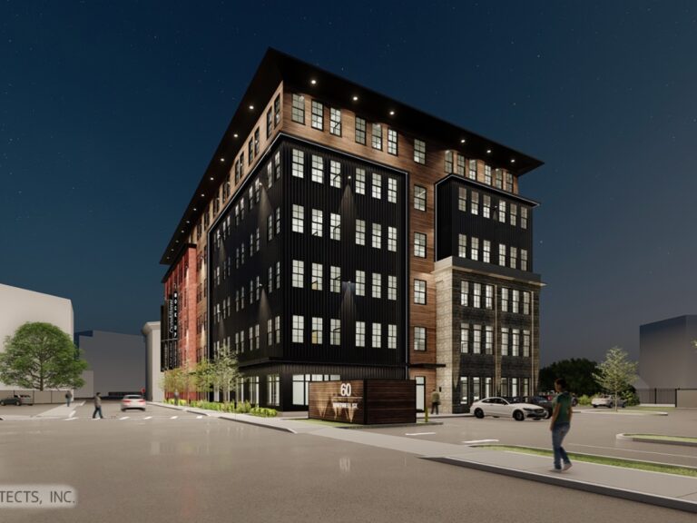 Modern multi-story building with a mix of wood and stone exterior, surrounded by trees and parked cars.