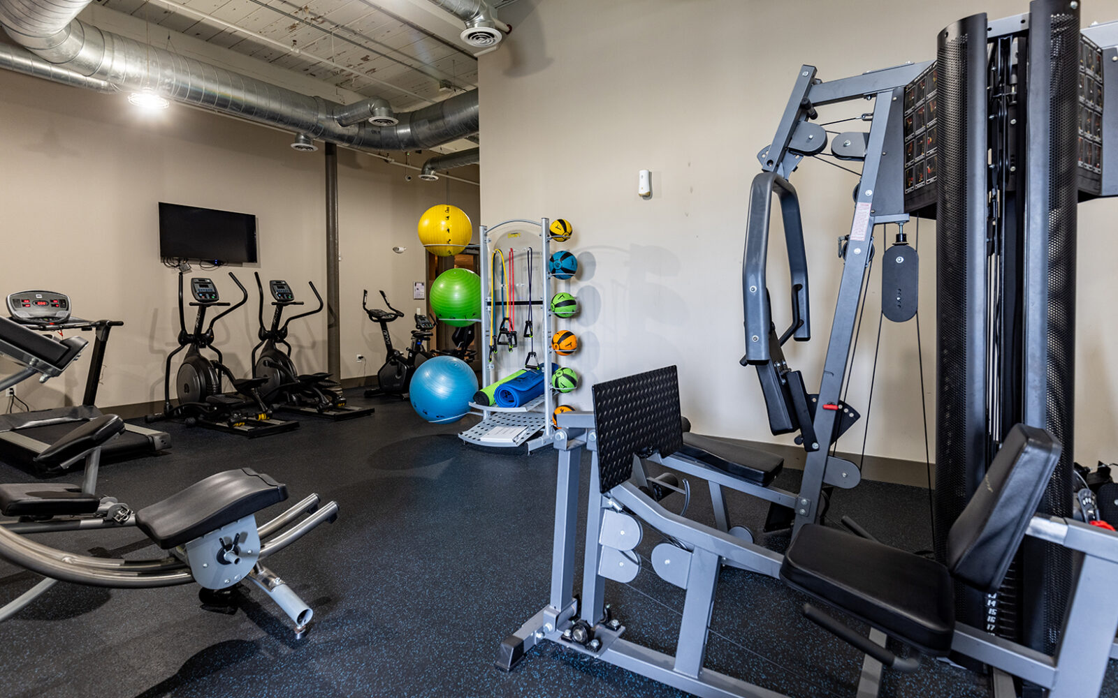A fitness room featuring exercise machines, weights, and colorful stability balls.