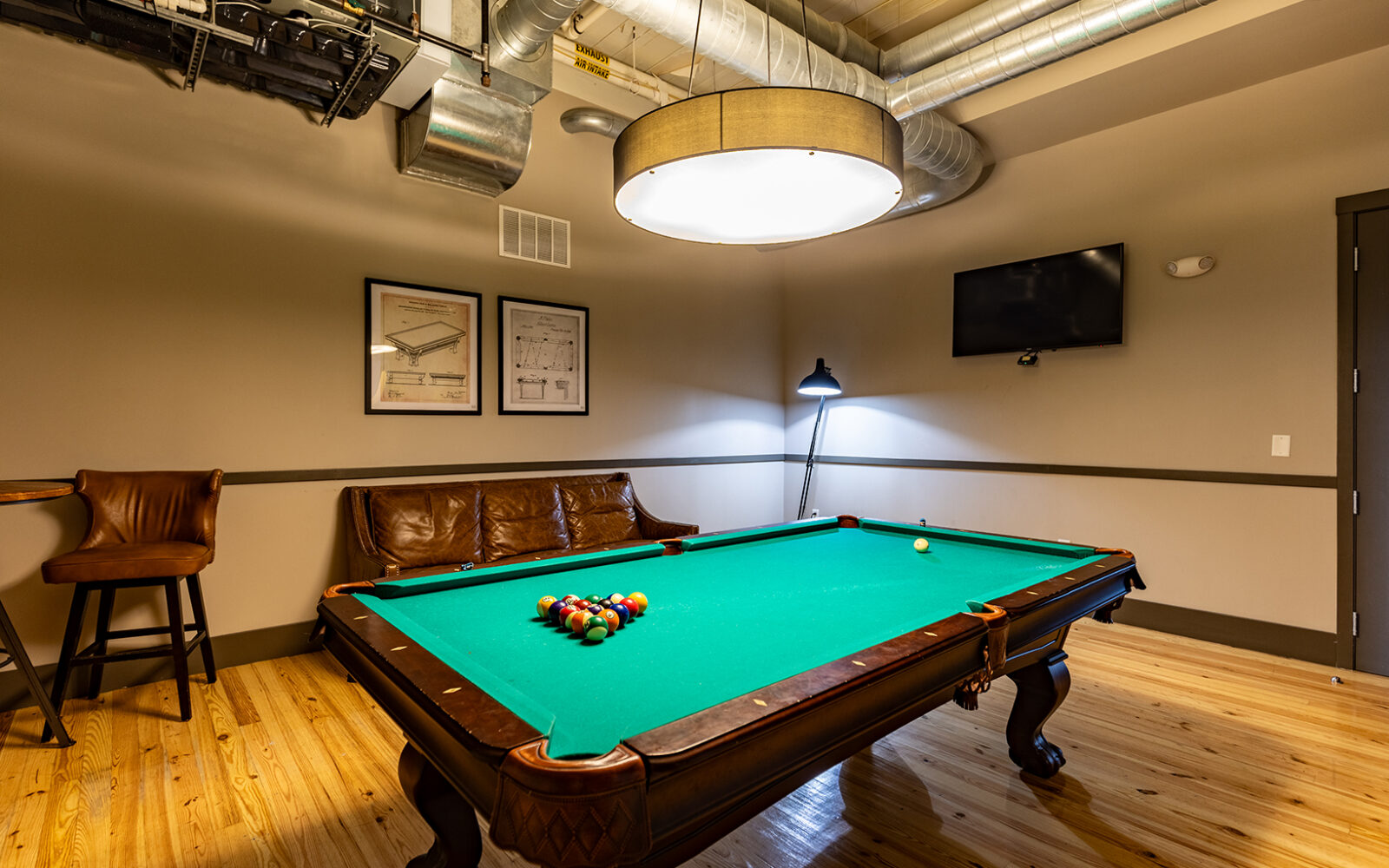 A pool table with balls arranged, a leather couch, and a lamp in a cozy room.