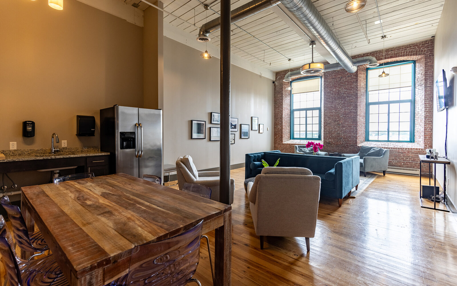 Spacious living area with a kitchen, dining table, and seating. Large windows illuminate the room.