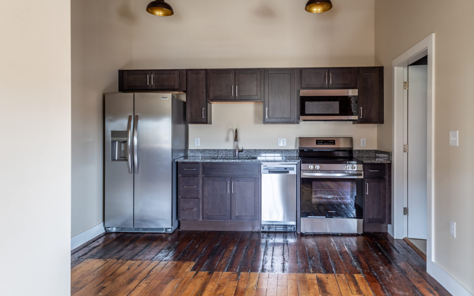 Modern kitchen with stainless steel appliances, dark cabinets, and wooden flooring.