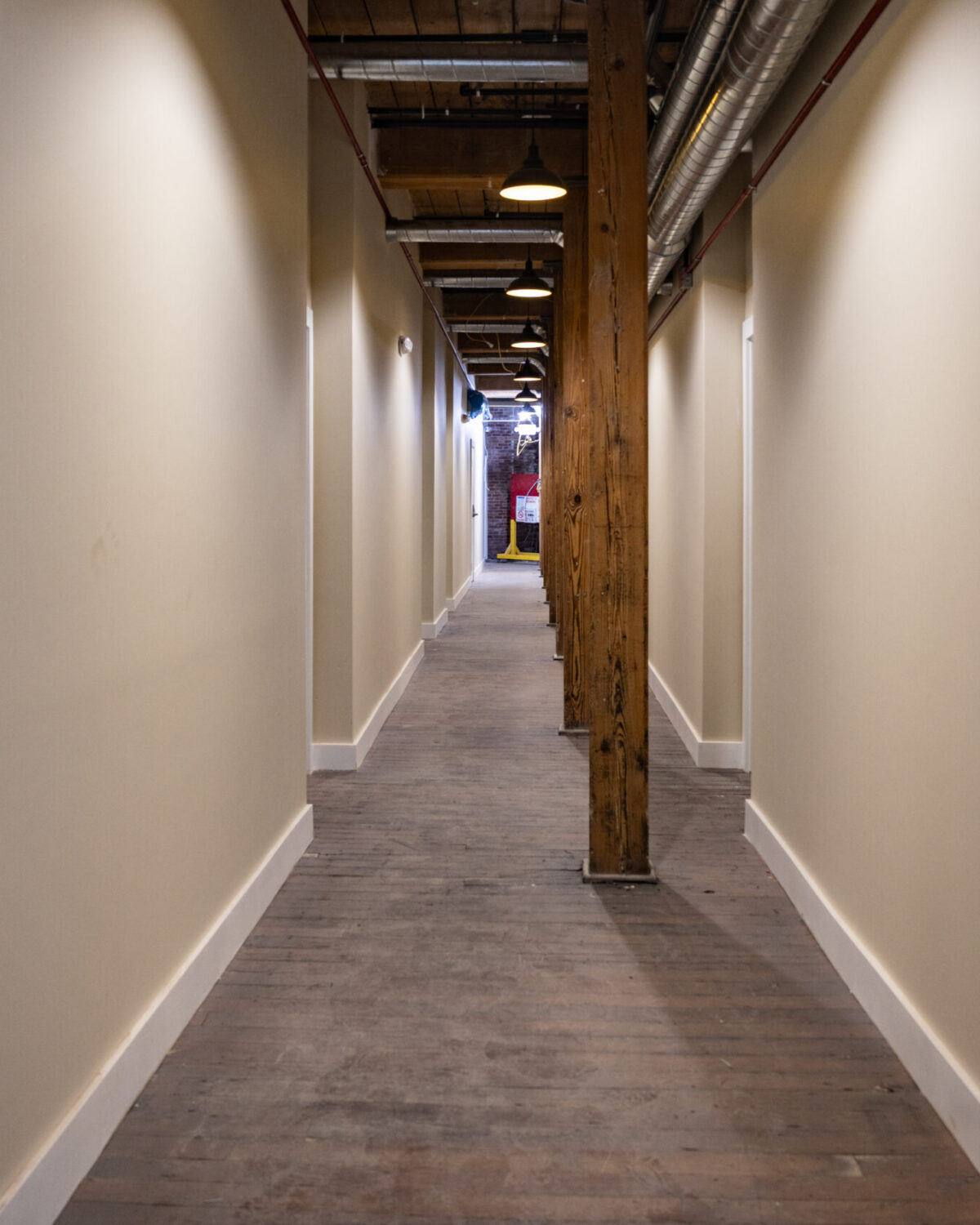 A long, narrow hallway with wooden floors and walls, featuring exposed beams and doors on either side.