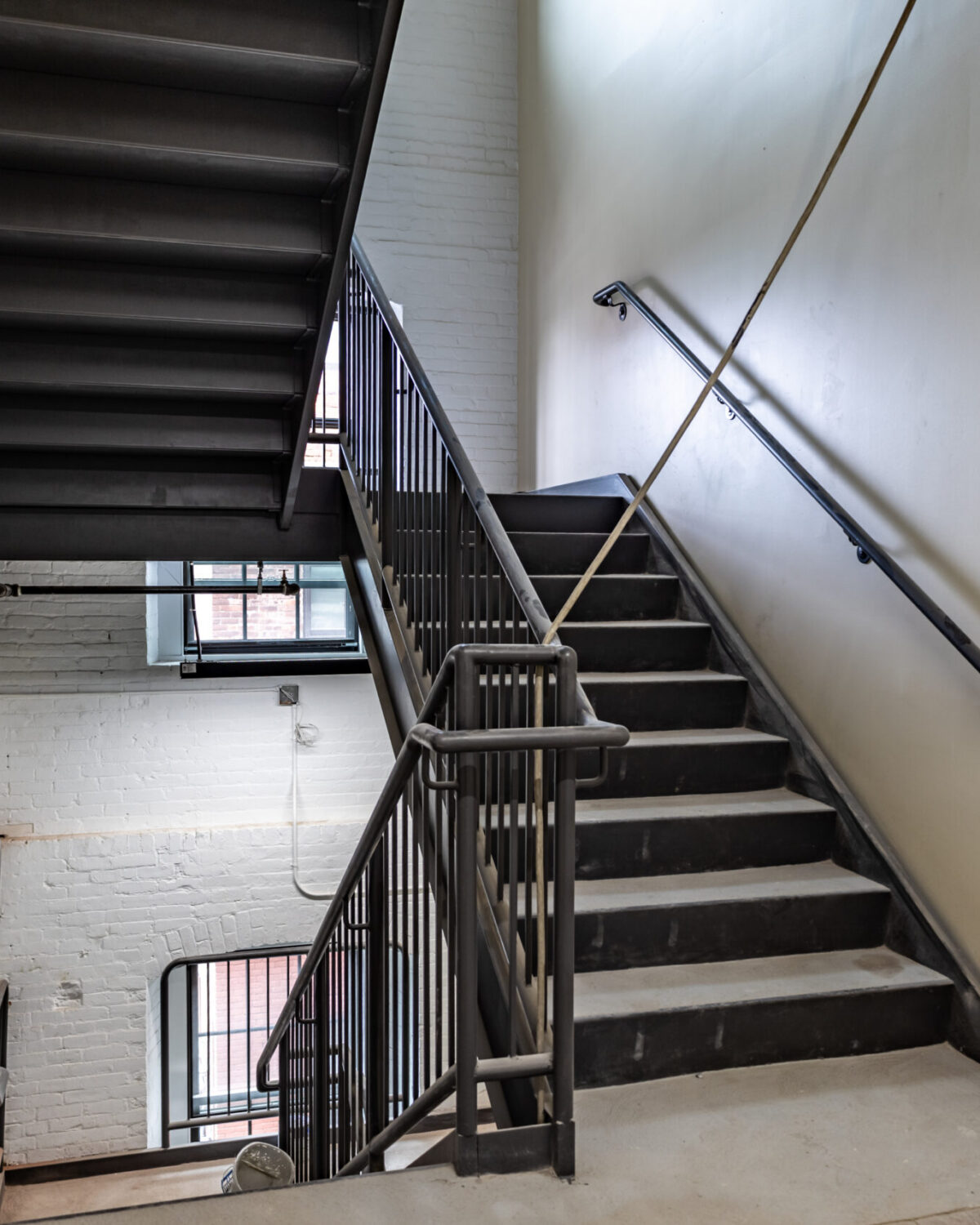Staircase with metal railings, leading to upper levels, surrounded by white brick walls and natural light.