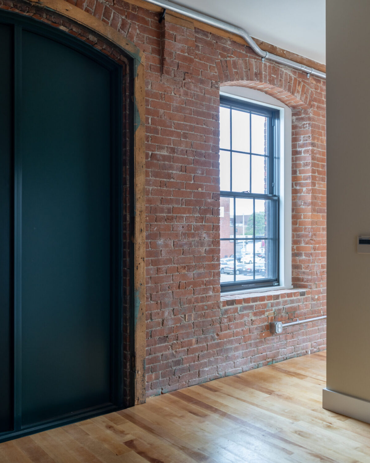 Room with exposed brick walls, large window, and sliding green door. Wooden floor and closet space visible.