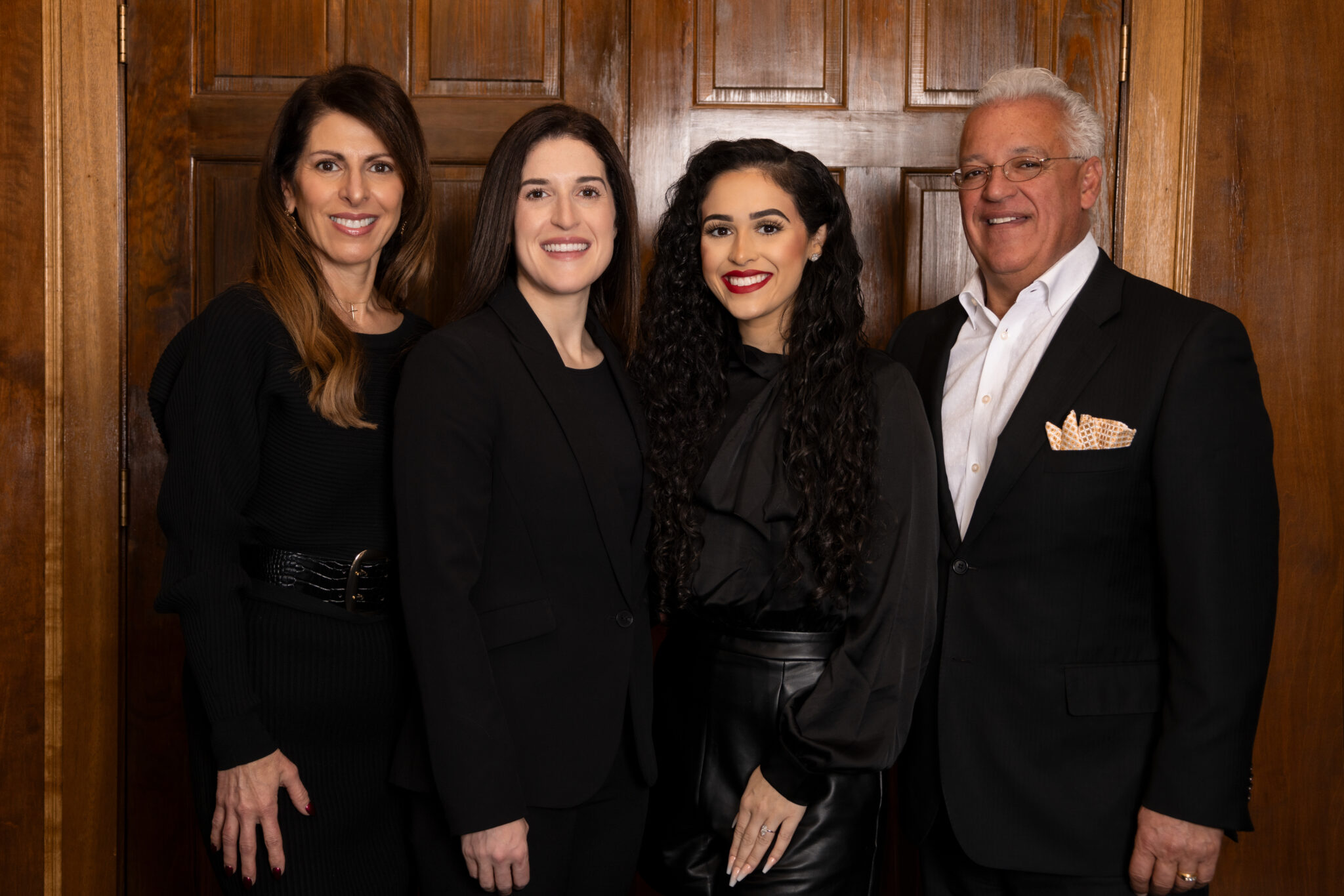 Four people pose together in formal attire, smiling in front of a wooden backdrop.