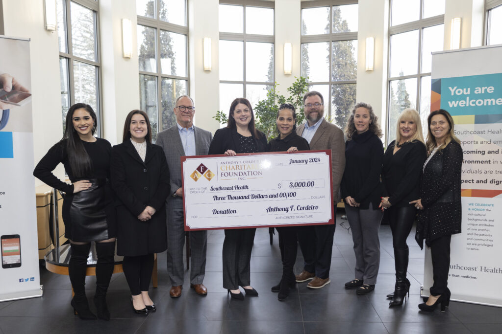 Group of people presenting a $3,000 donation check to Southcoast Health in a bright, welcoming space.