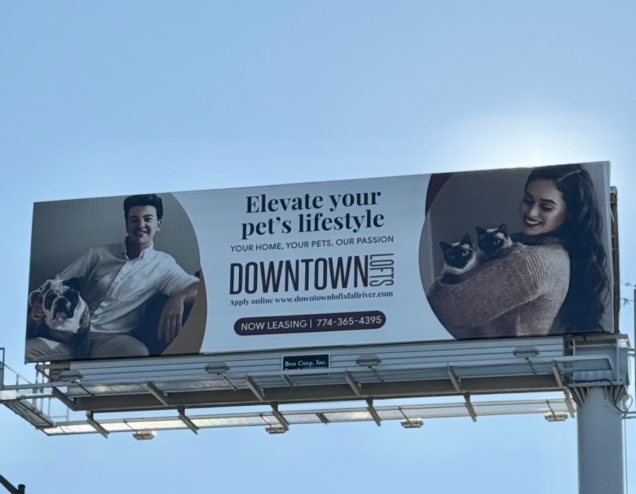 Billboard promoting pet-friendly apartments. A man holds a dog, and a woman cuddles two cats.