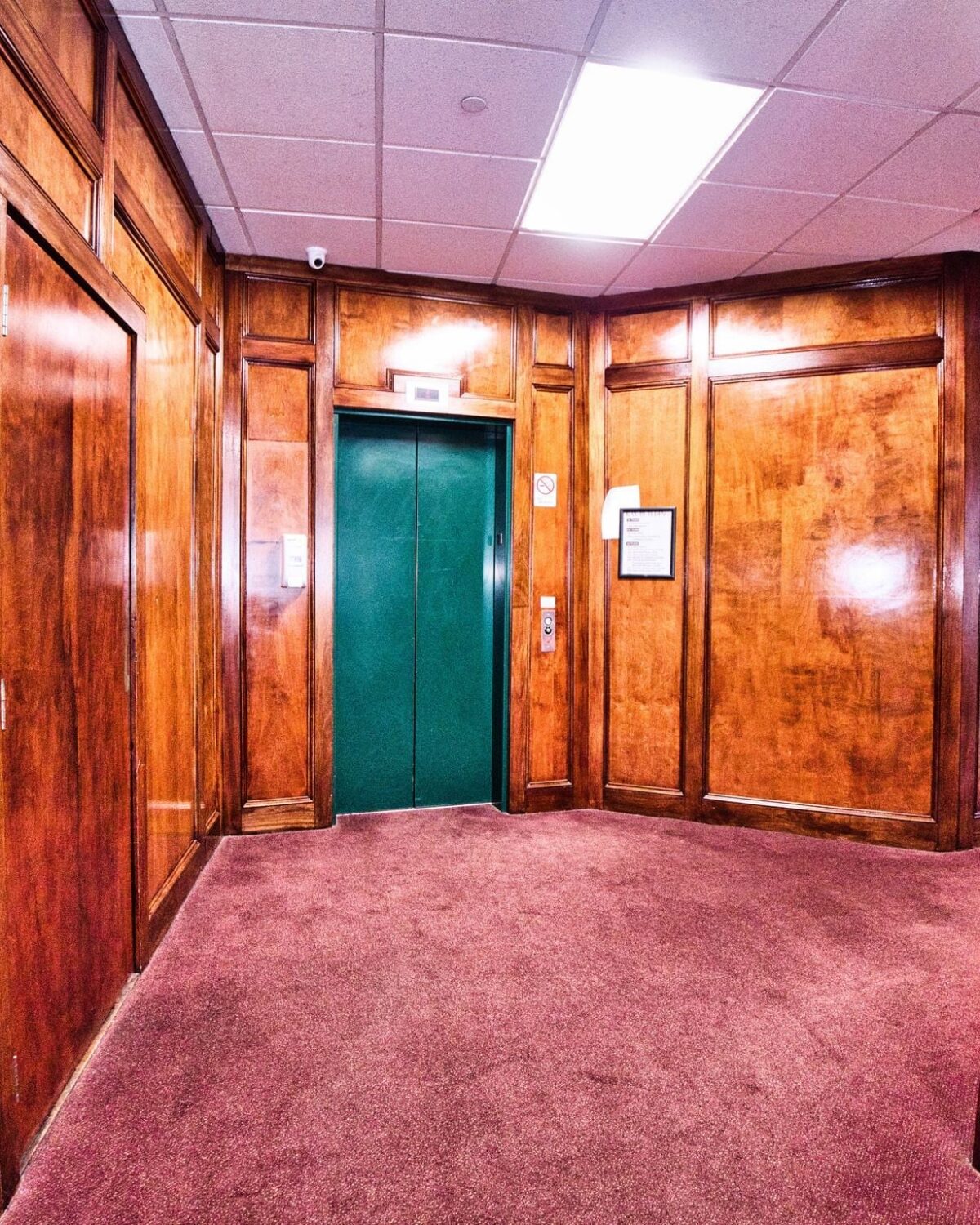 Wood-paneled elevator lobby with a green elevator door and carpeted floor.