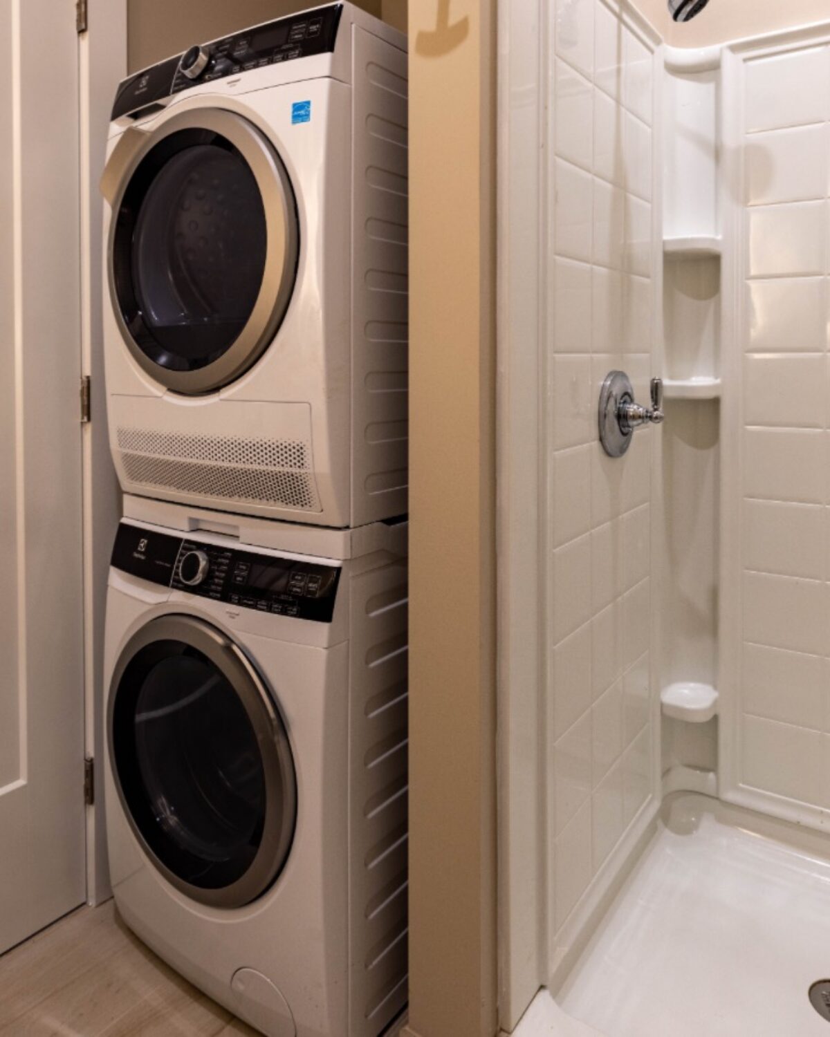 Stacked washer and dryer next to a white shower stall in a small laundry area.