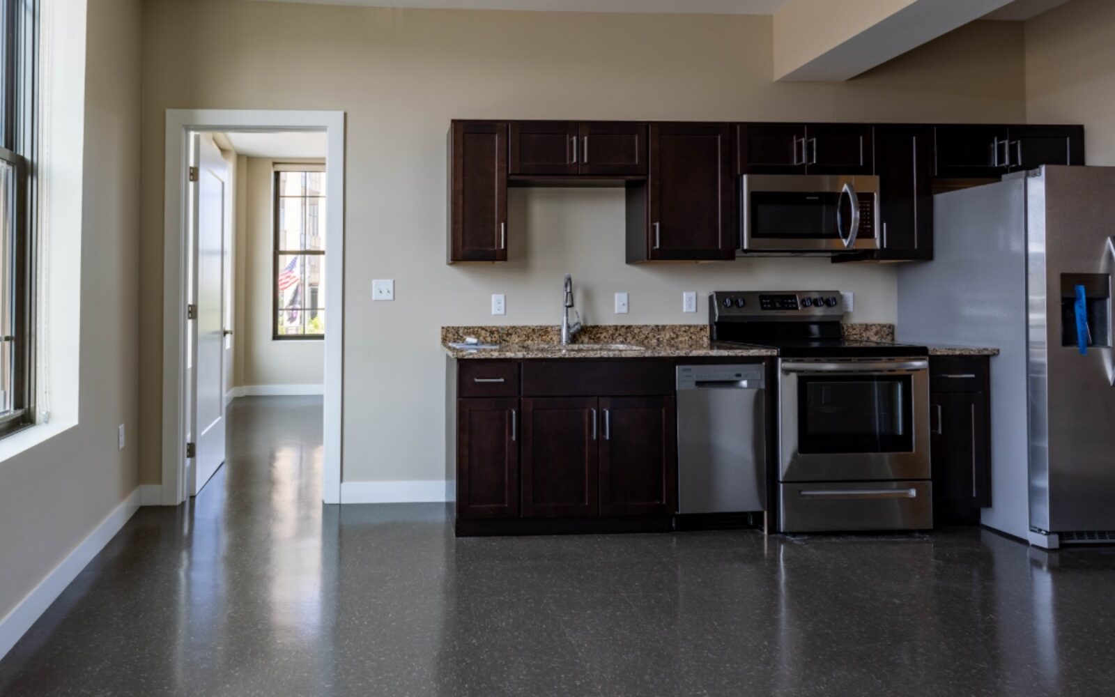 Modern kitchen with dark cabinets, stainless steel appliances, and a doorway leading to another room.