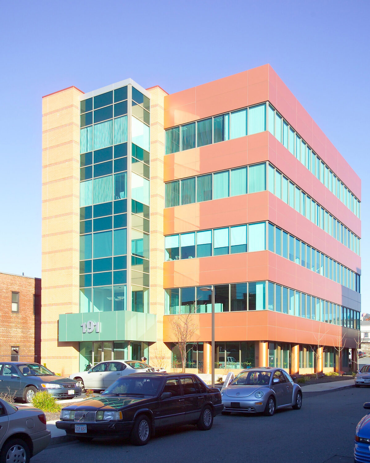Modern MelCor Building 1 features colorful glass and brick exterior, surrounded by parked cars.