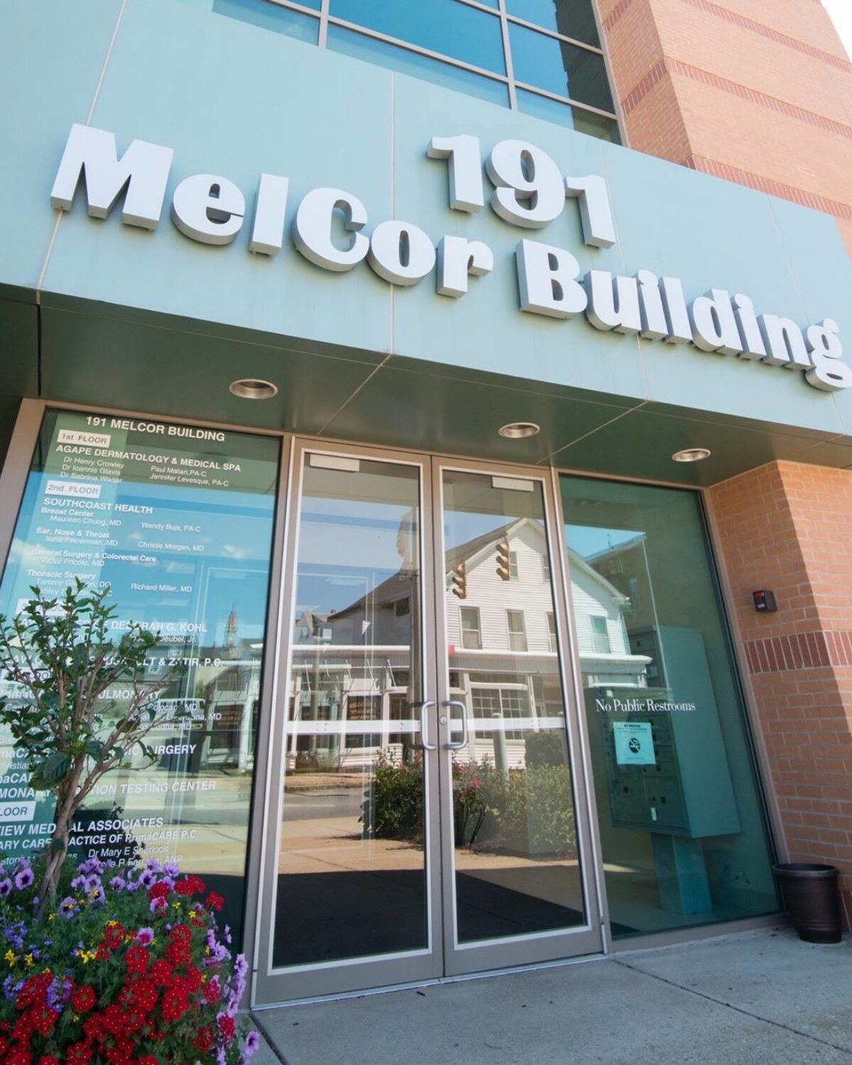 Entrance of MelCor Building with glass doors, signage for medical services, and flower beds.