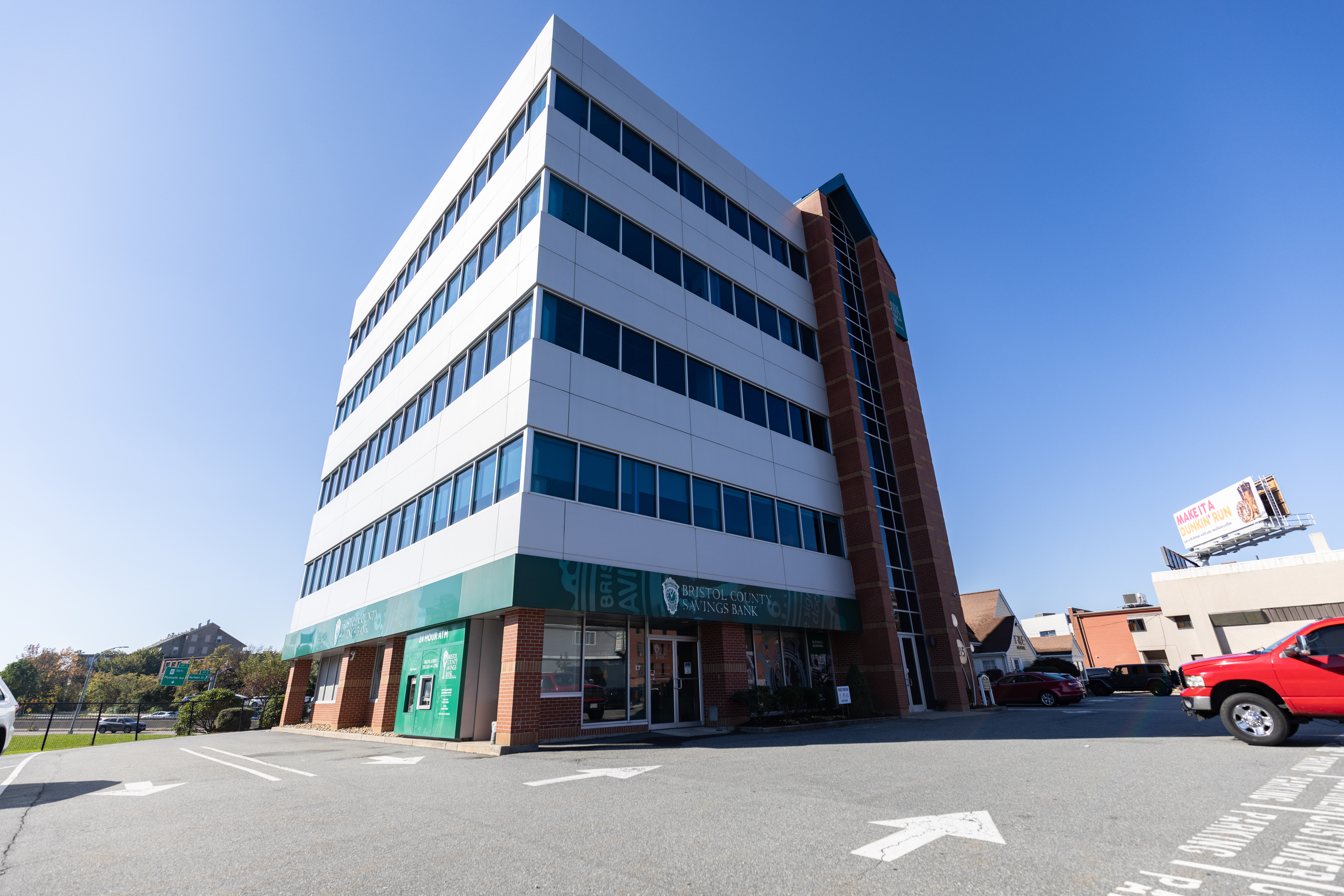 Five-story bank building with large windows and an ATM in front, clear blue sky above.