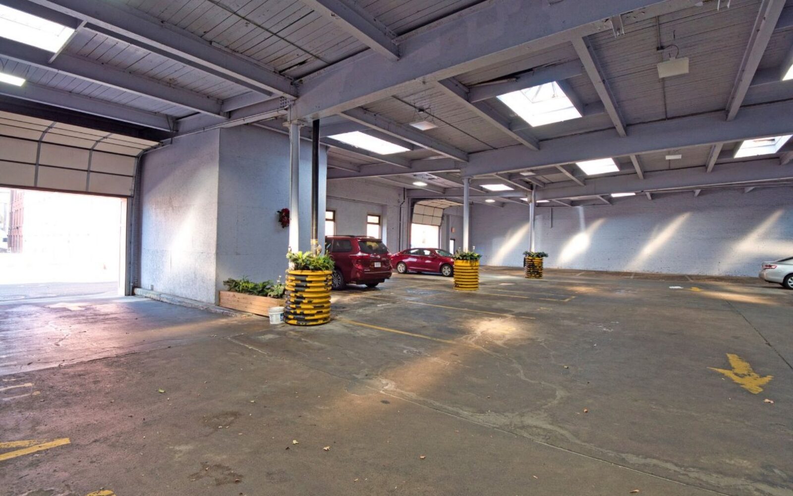 Spacious parking area with several cars and yellow-striped planters. Natural light from skylights.