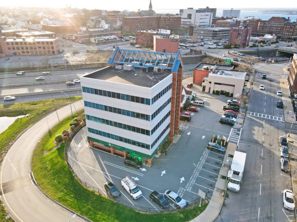 Aerial view of a multi-story building with parking, surrounded by roads and cityscape.