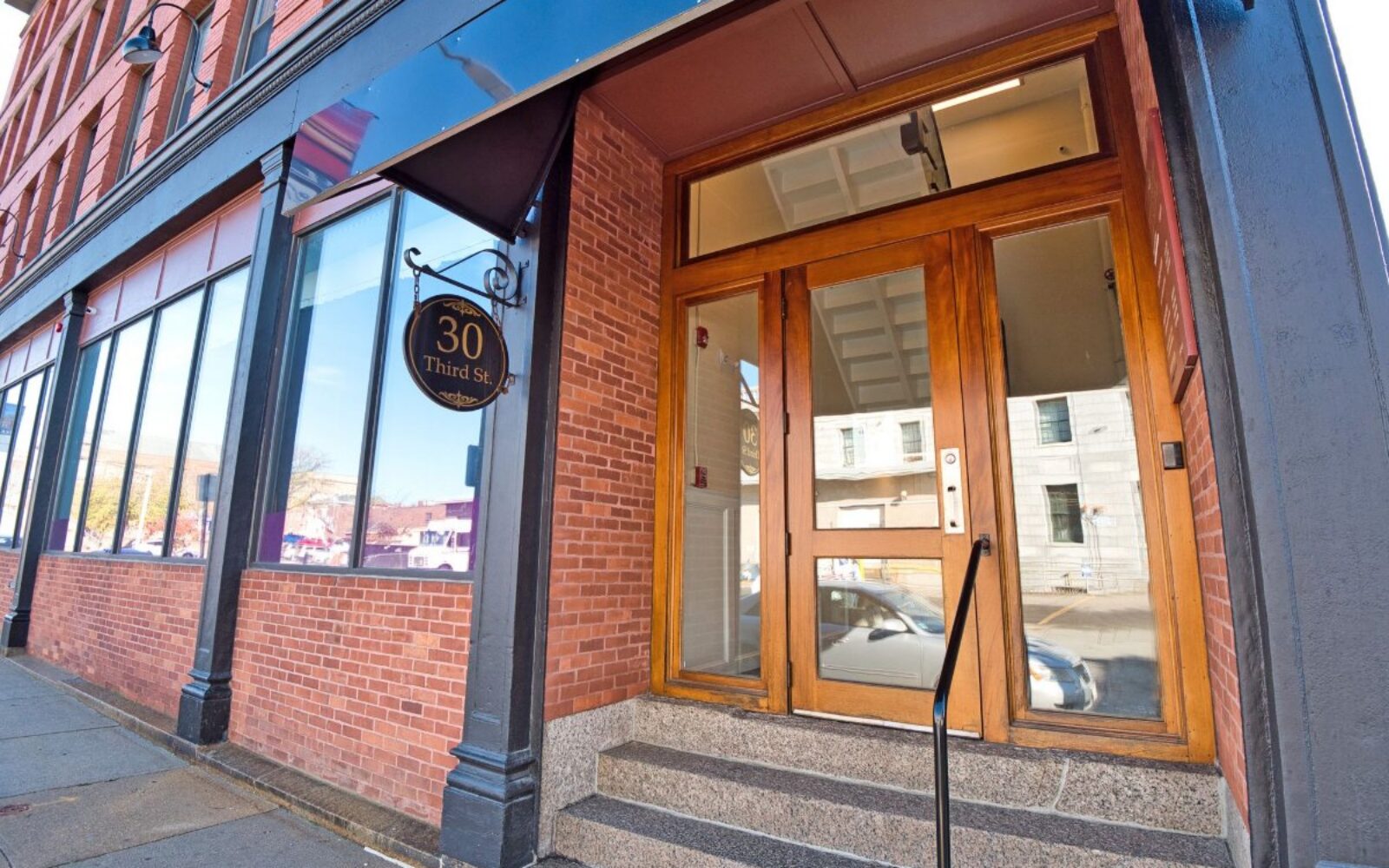 Entrance to a brick building with large windows and a sign reading "30 Third St." Steps lead to the door.