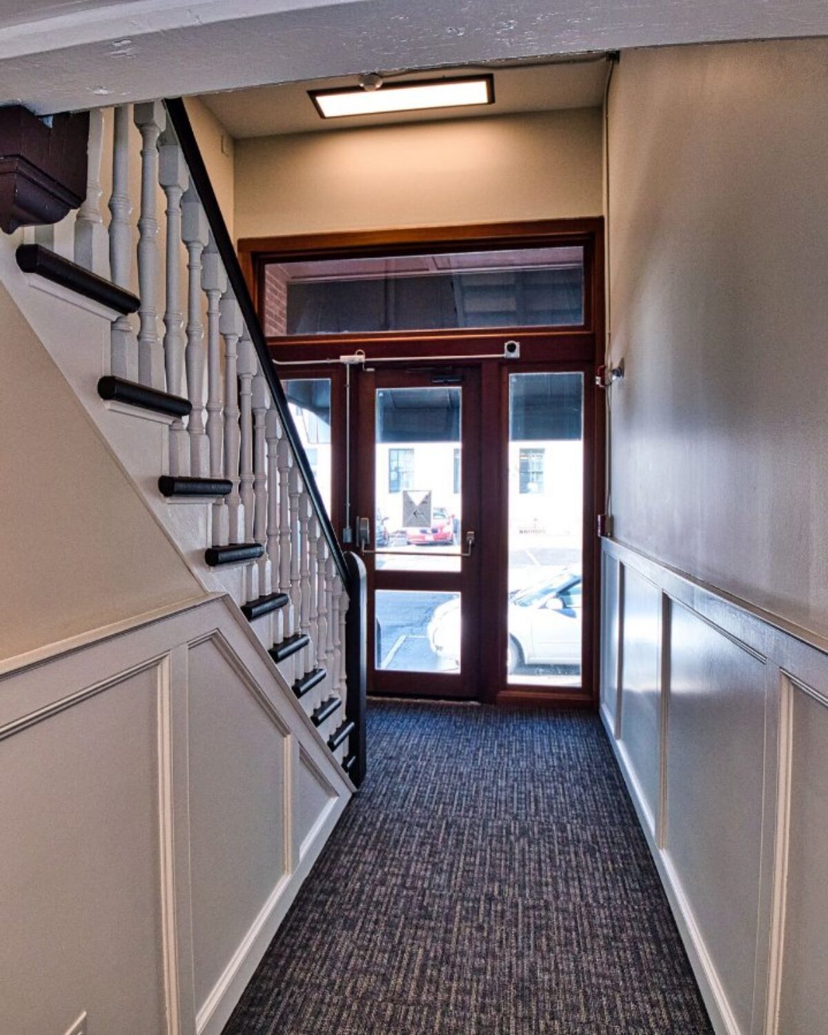 Hallway with stairs on the left and a glass door leading outside at the end.