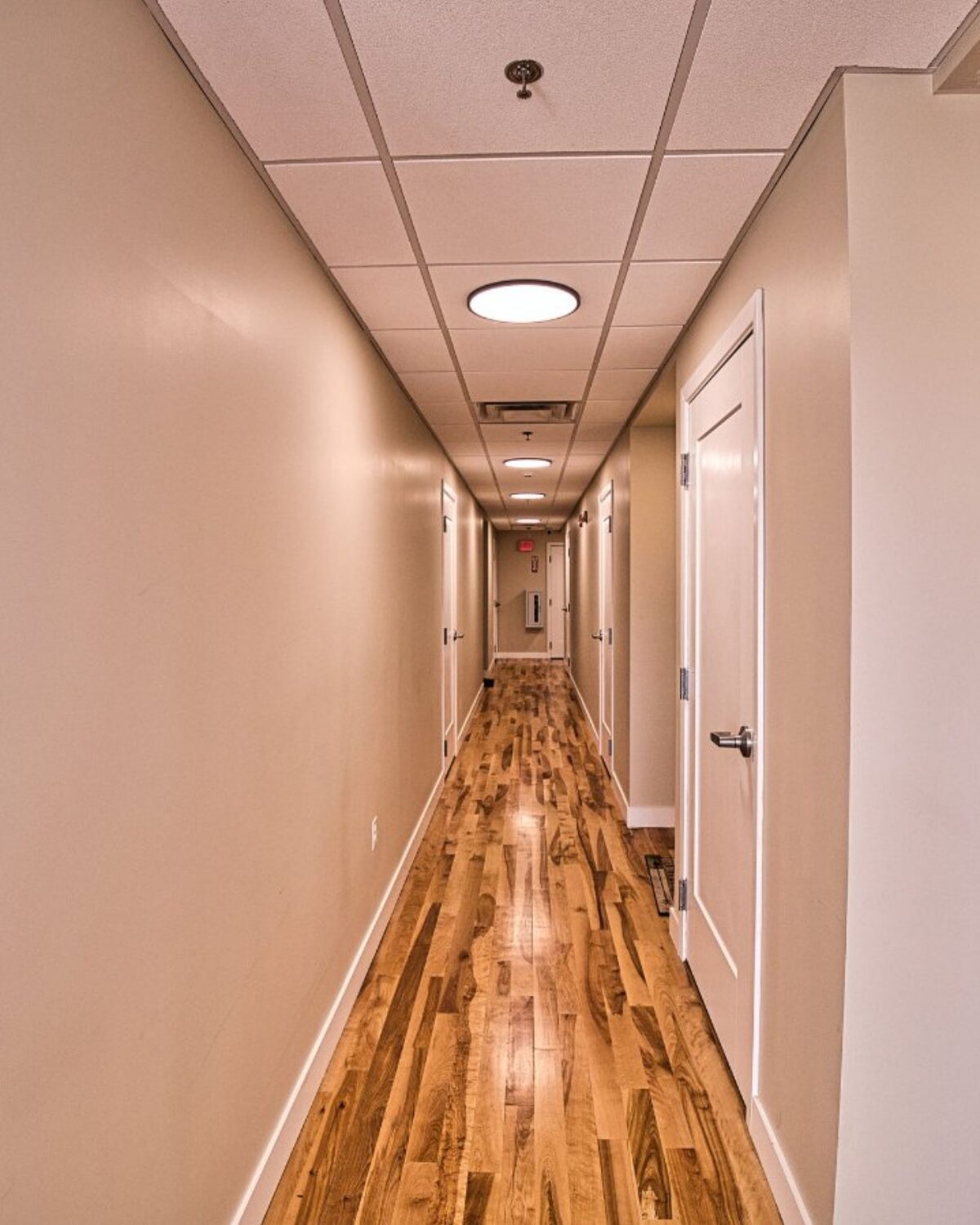 Long hallway with wooden flooring, light fixtures, and several closed doors on either side.