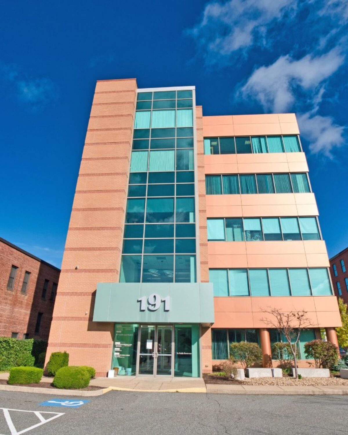 Modern five-story building with large windows, featuring a prominent entrance and landscaped surroundings.