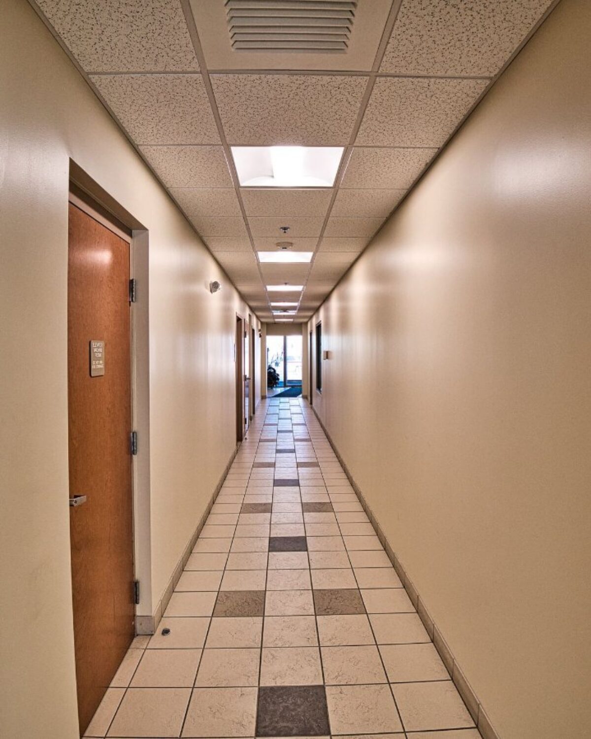 Long, well-lit hallway with doors on both sides and a view of the exit at the end.