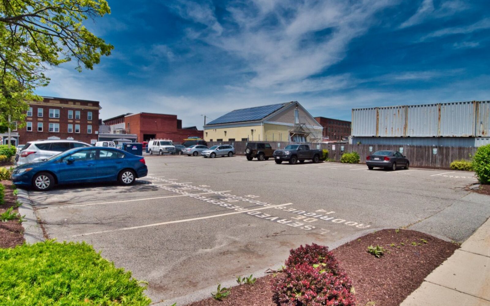 Parking lot with several cars, buildings in the background, and a clear blue sky.