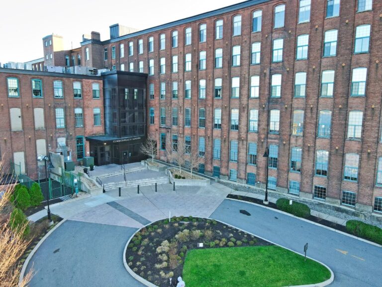 Brick building with large windows, entrance sign, landscaped courtyard, and walking path.