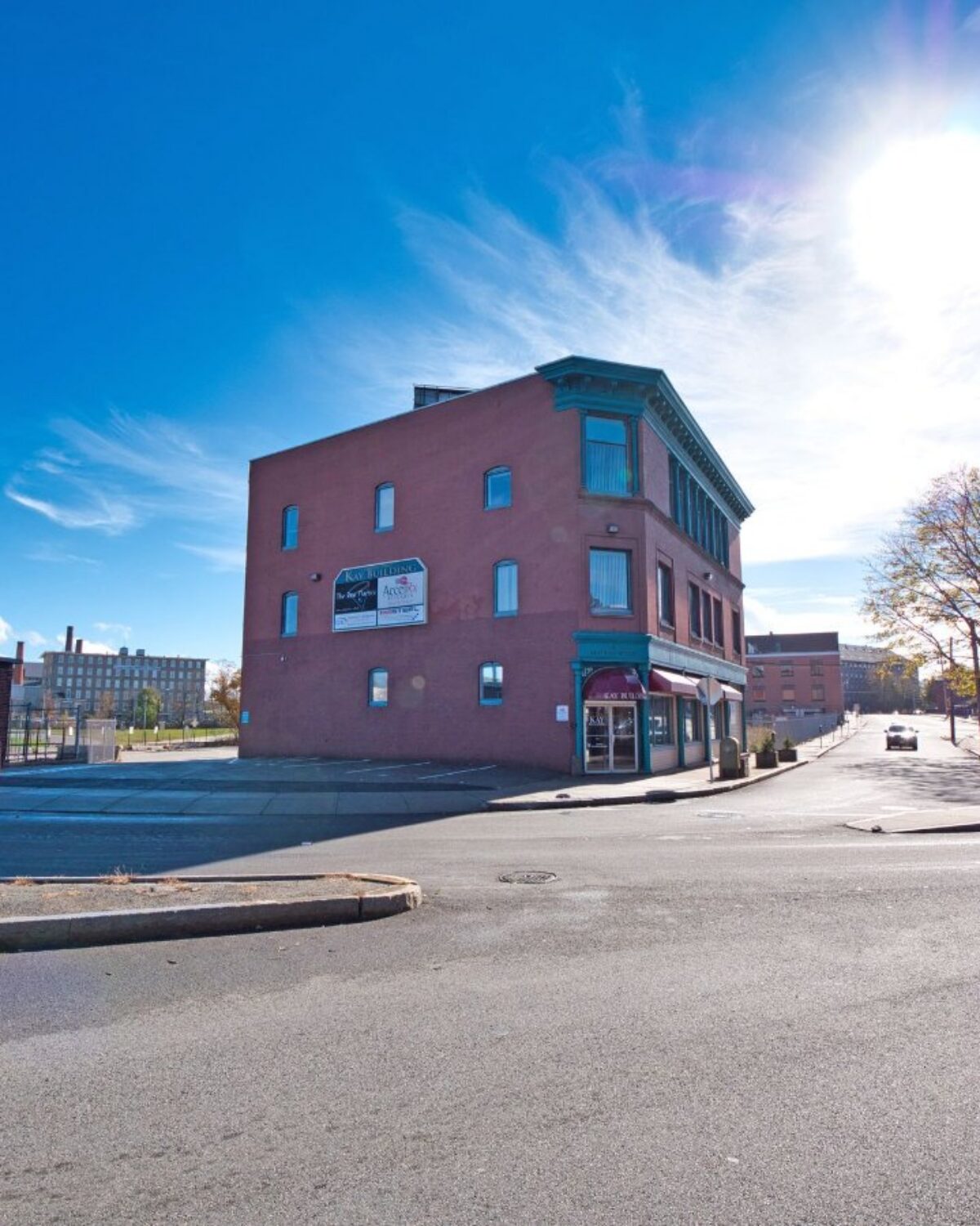 Street view of a corner building with large windows and signage, surrounded by other structures and a clear blue sky.