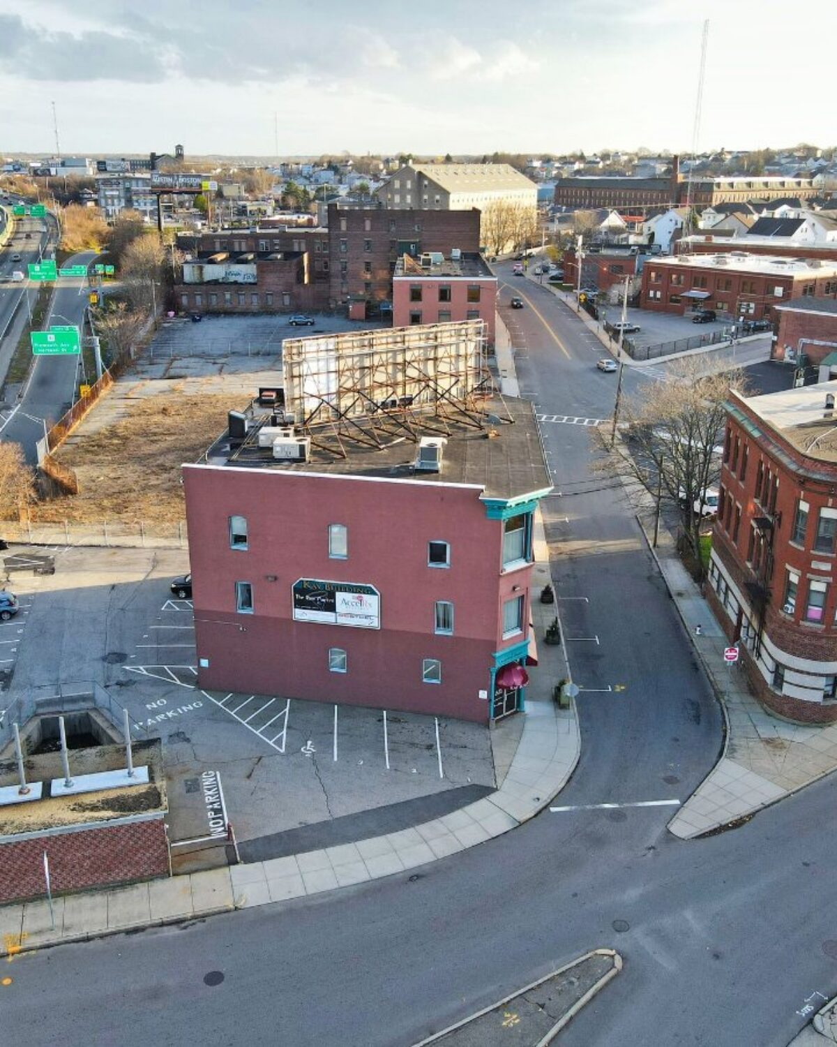 Aerial view of a city intersection with buildings, a highway, and vacant land.