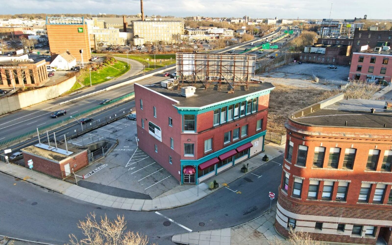 Aerial view of a red brick building with a sign, surrounded by roads and vacant lots.
