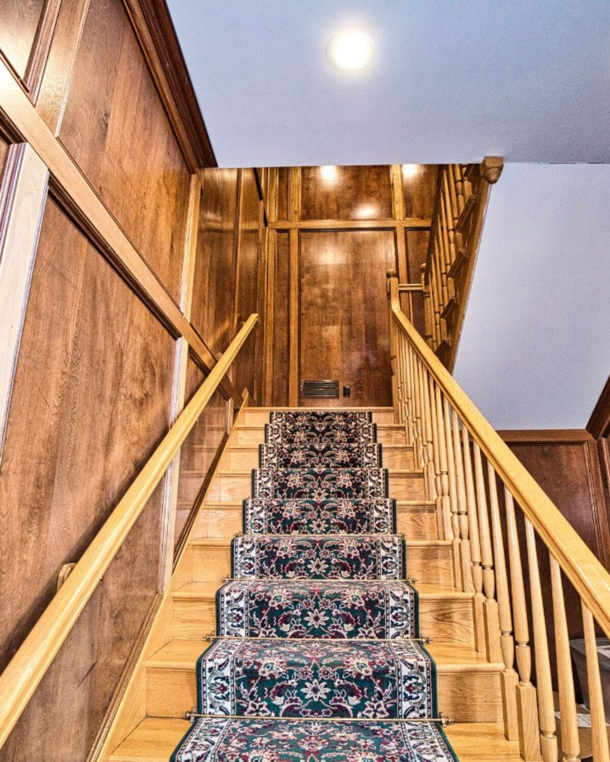 Wooden staircase with a patterned carpet runner, leading to a well-lit upper landing.