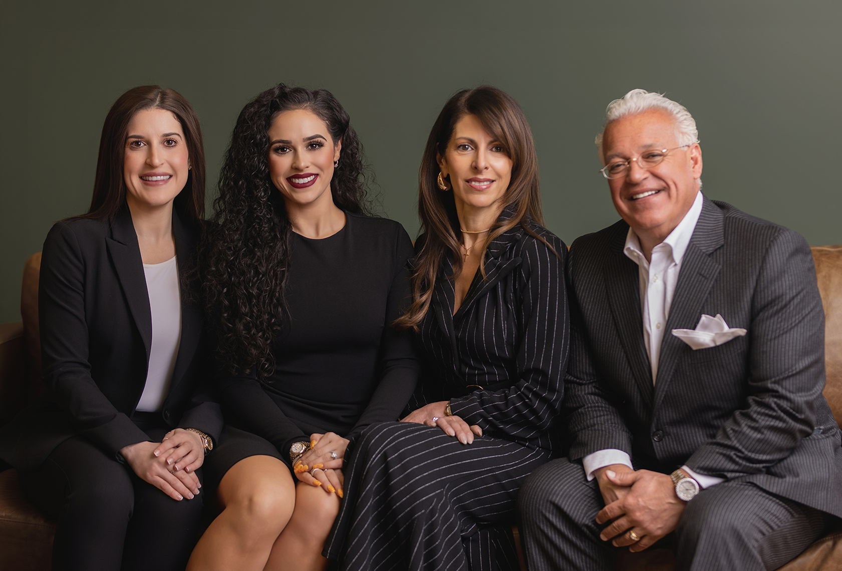 Four professionals pose together on a couch, smiling and dressed in business attire.