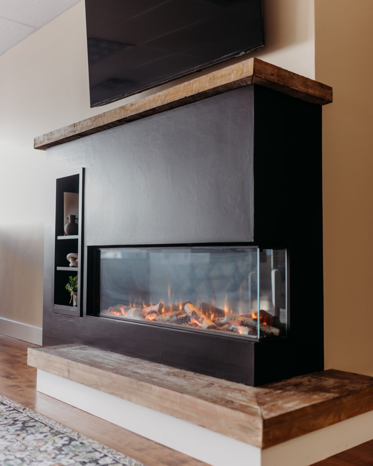 Modern fireplace with a glass front, wooden mantel, and a television mounted above.