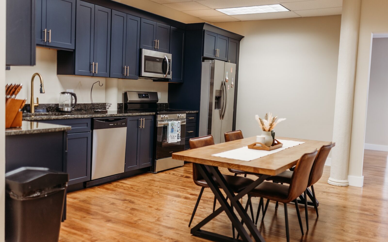 Modern kitchen with navy cabinets, stainless steel appliances, and a wooden dining table set for four.