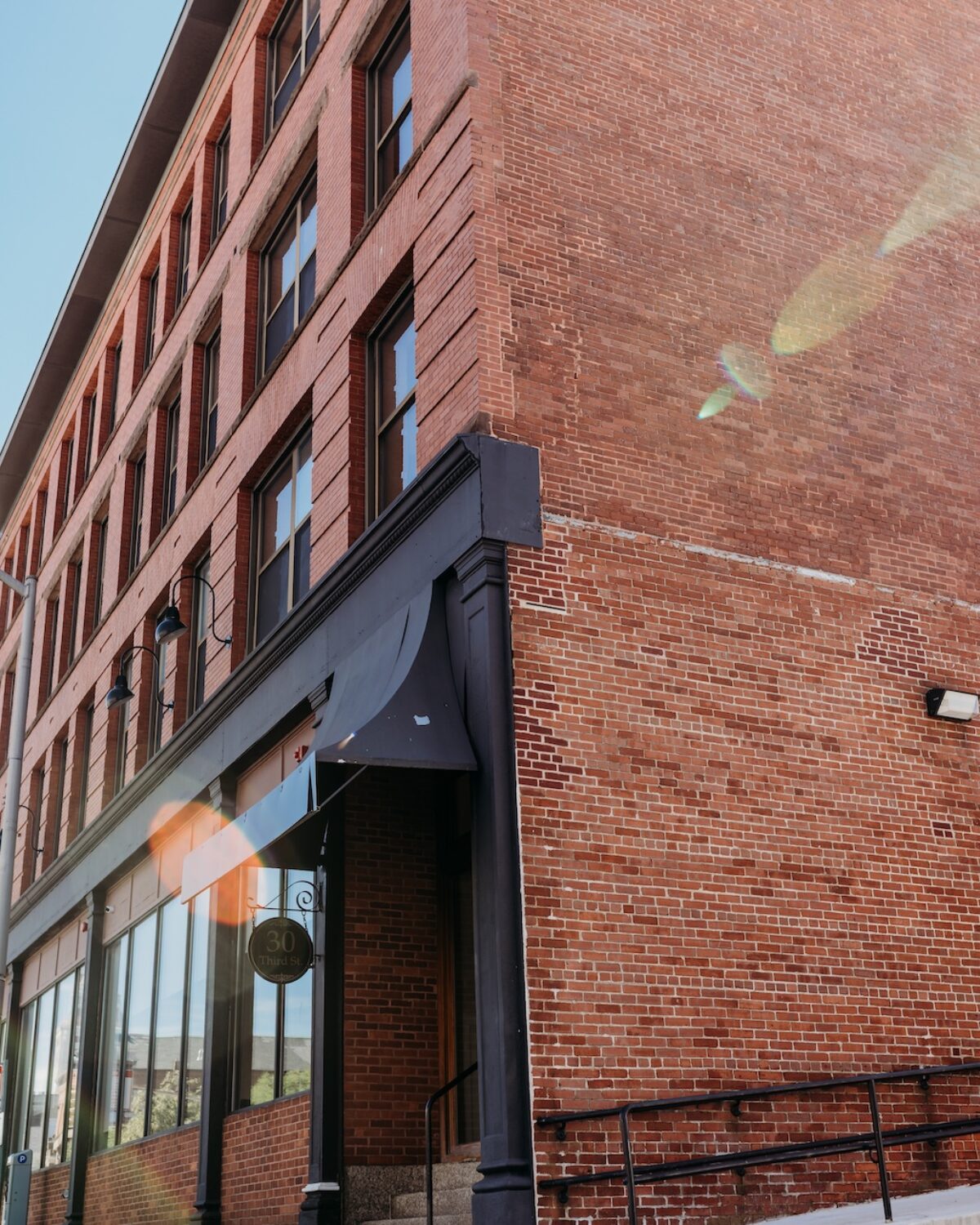 Brick building corner with large windows, entrance steps, and a ramp. Sign reads "30 Third St.