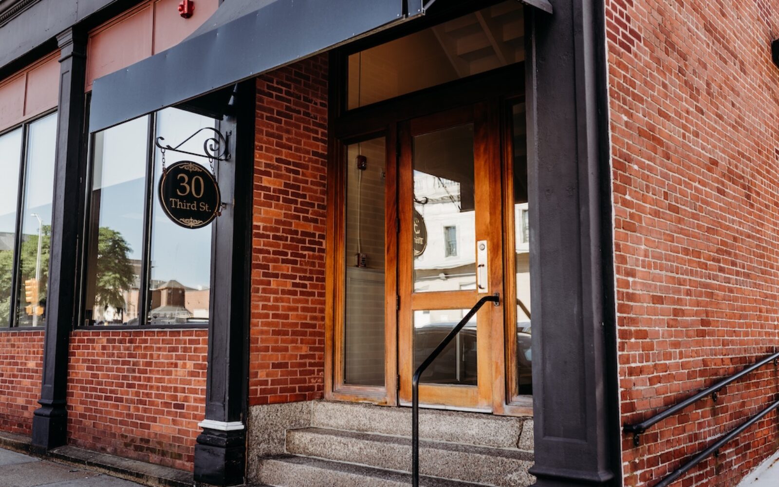 Brick building entrance with wooden doors and a sign reading "30 Third St." Steps lead up to the door.