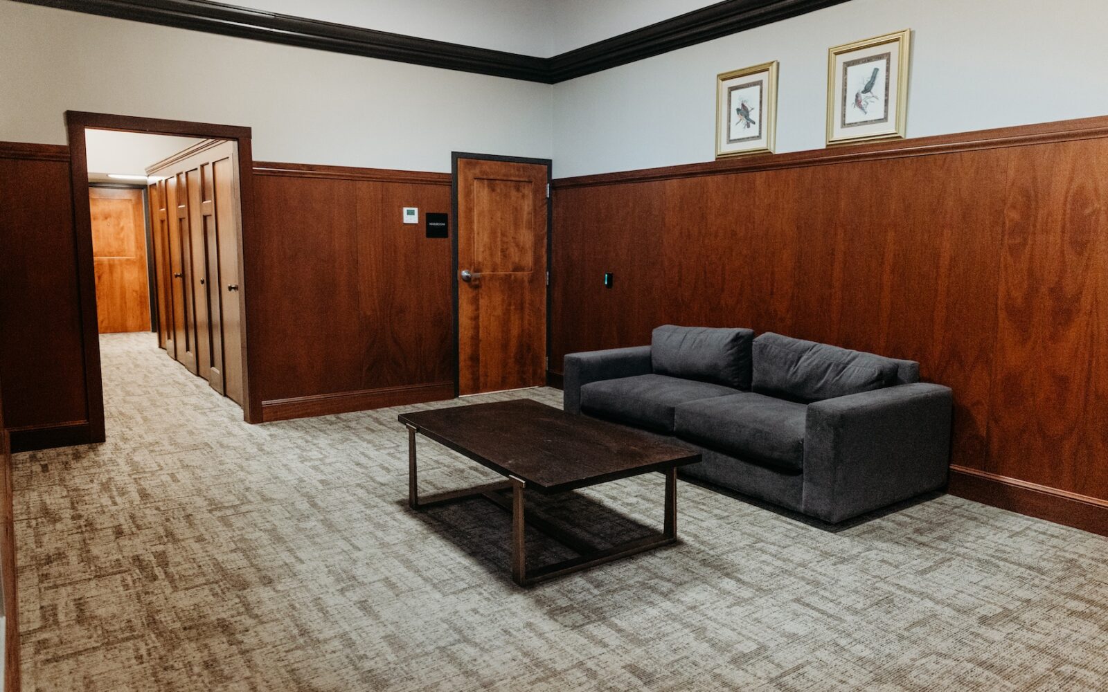 A cozy room with a gray sofa, wooden walls, and a coffee table. Two doors lead to other areas.