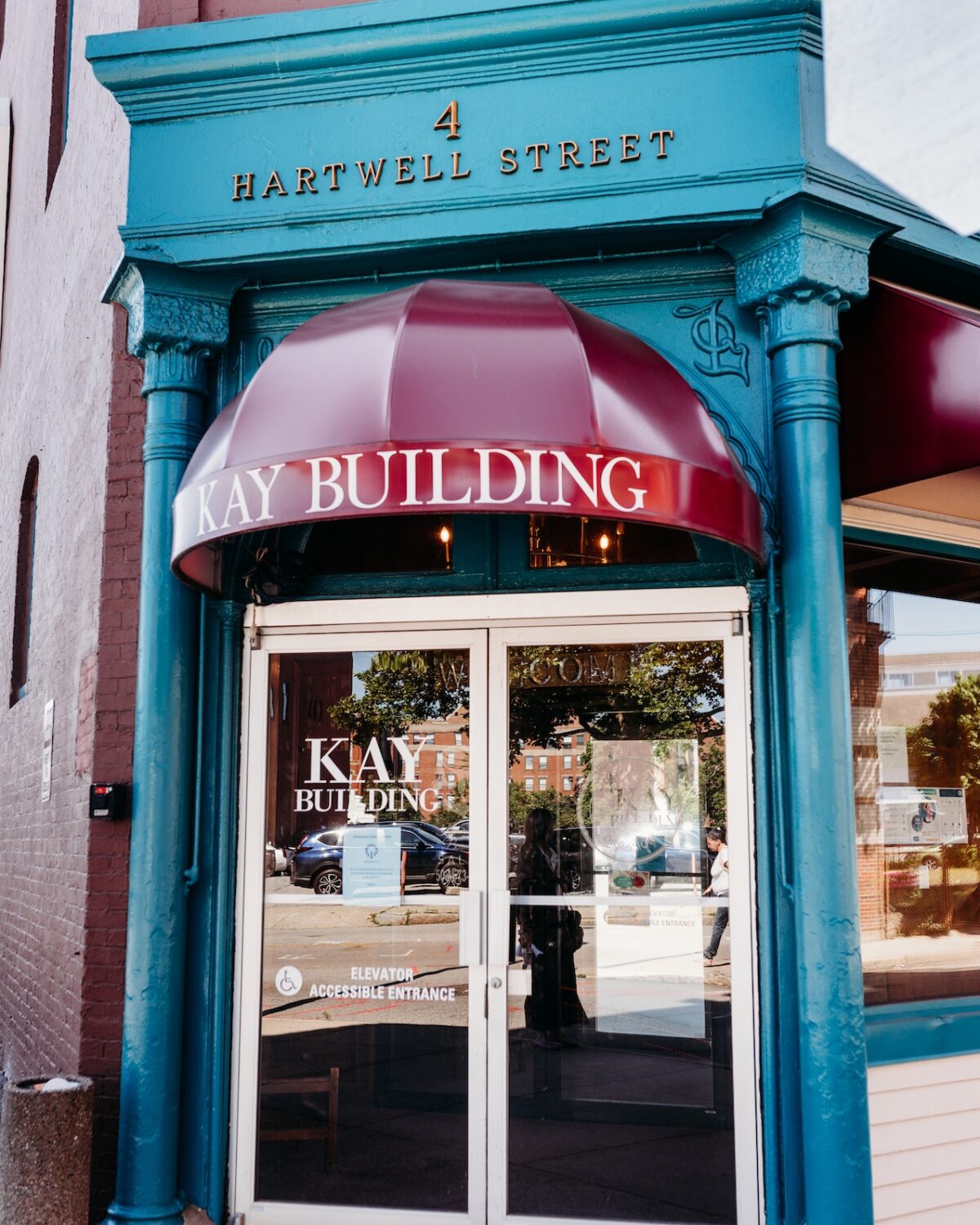 Entrance of the Kay Building on Hartwell Street, featuring a maroon awning and accessible entrance sign.