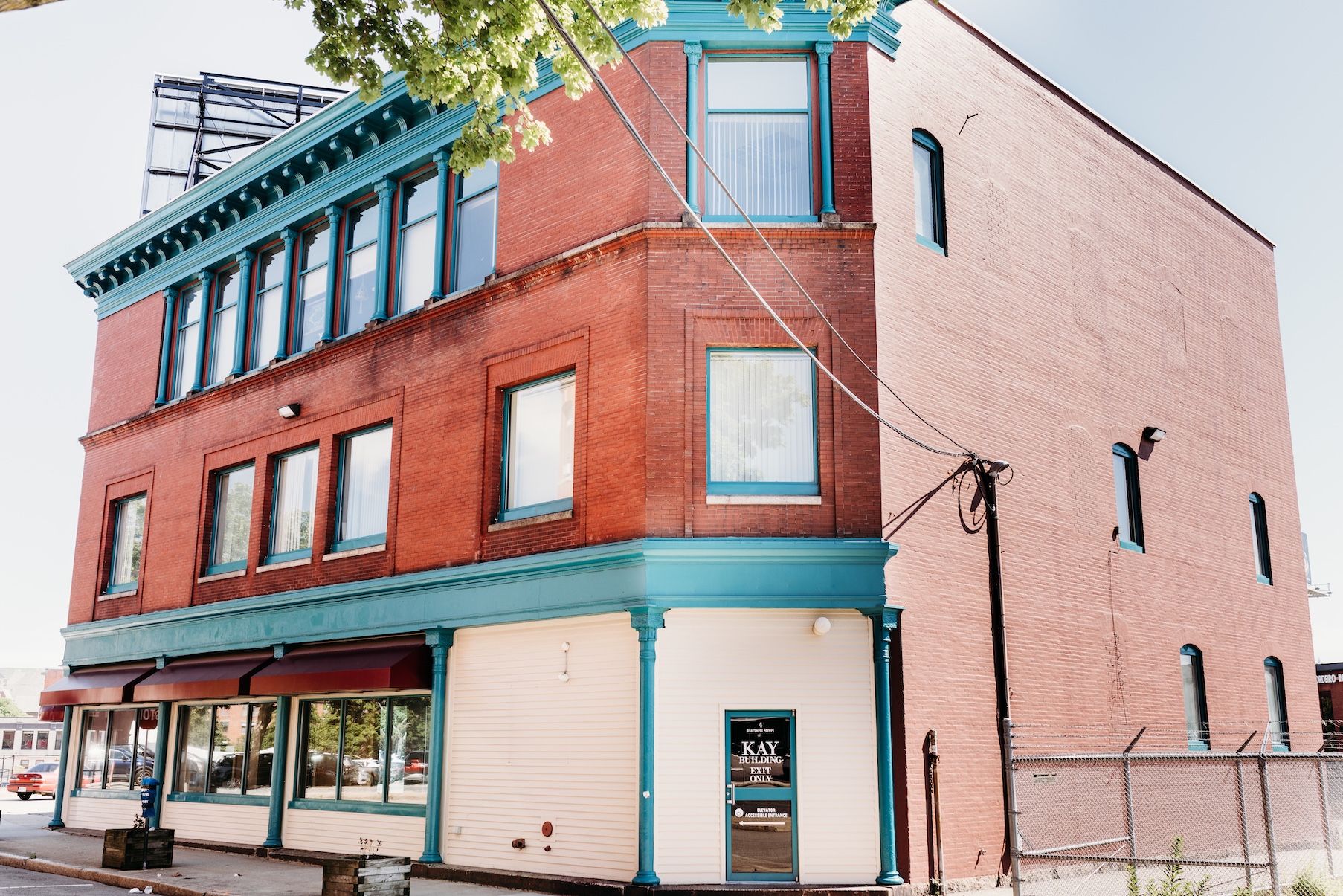 Red brick building with teal accents, large windows, and a sign for "KAY BUILDING EXIT.