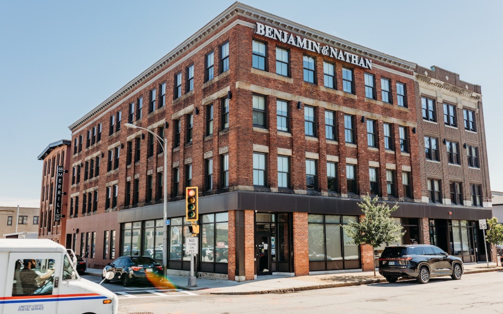 Brick building with "BENJAMIN & NATHAN" sign, traffic light, and parked cars on a sunny day.