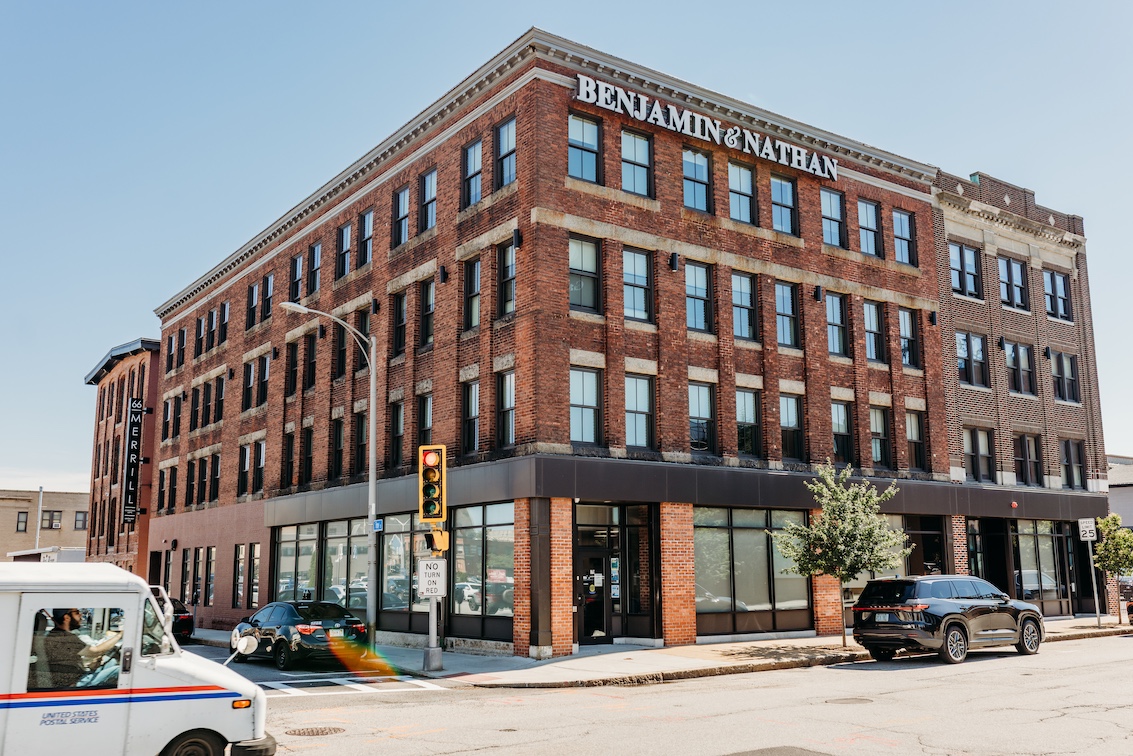 Brick building with "BENJAMIN & NATHAN" sign, traffic light, and parked cars on a sunny day.