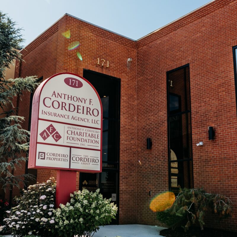 Sign for Anthony F. Cordeiro Insurance Agency outside a brick building, surrounded by greenery.