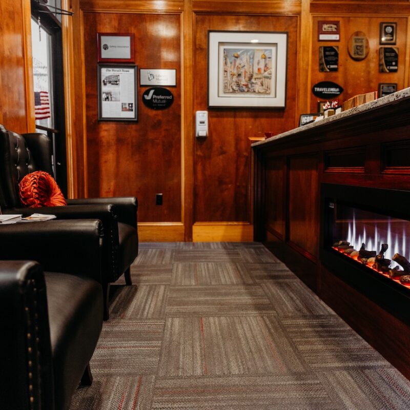 Cozy reception area with black chairs, orange cushions, a wooden counter, and an electric fireplace.