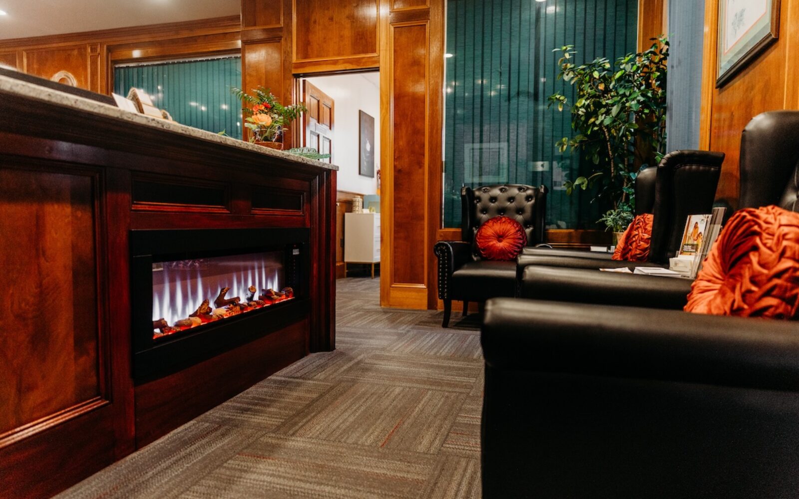 A cozy waiting area with a modern fireplace, black leather chairs, and green curtains.