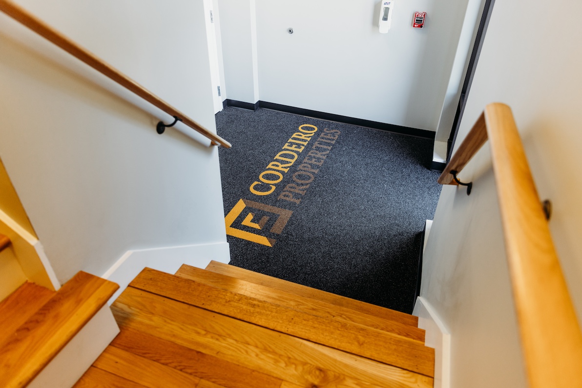 Wooden stairs lead down to a carpeted landing with "Cordeiro Properties" logo.