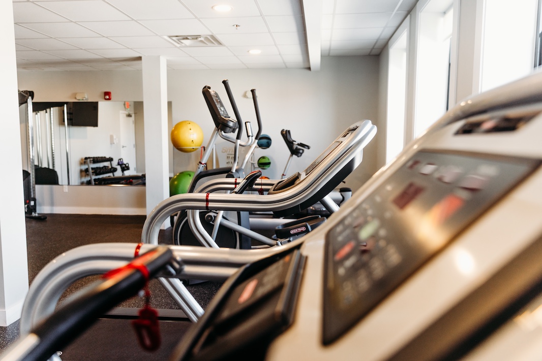Fitness equipment, including ellipticals, in a bright gym with exercise balls in the background.