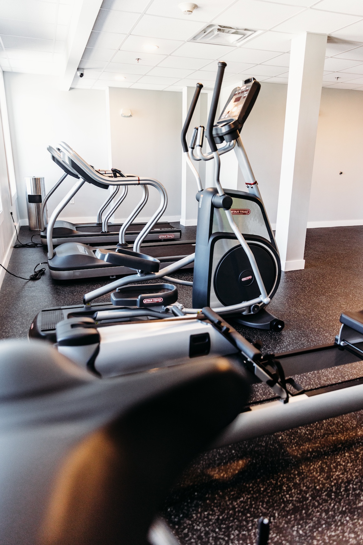 A fitness area featuring multiple elliptical machines and a rowing machine on a rubber floor.